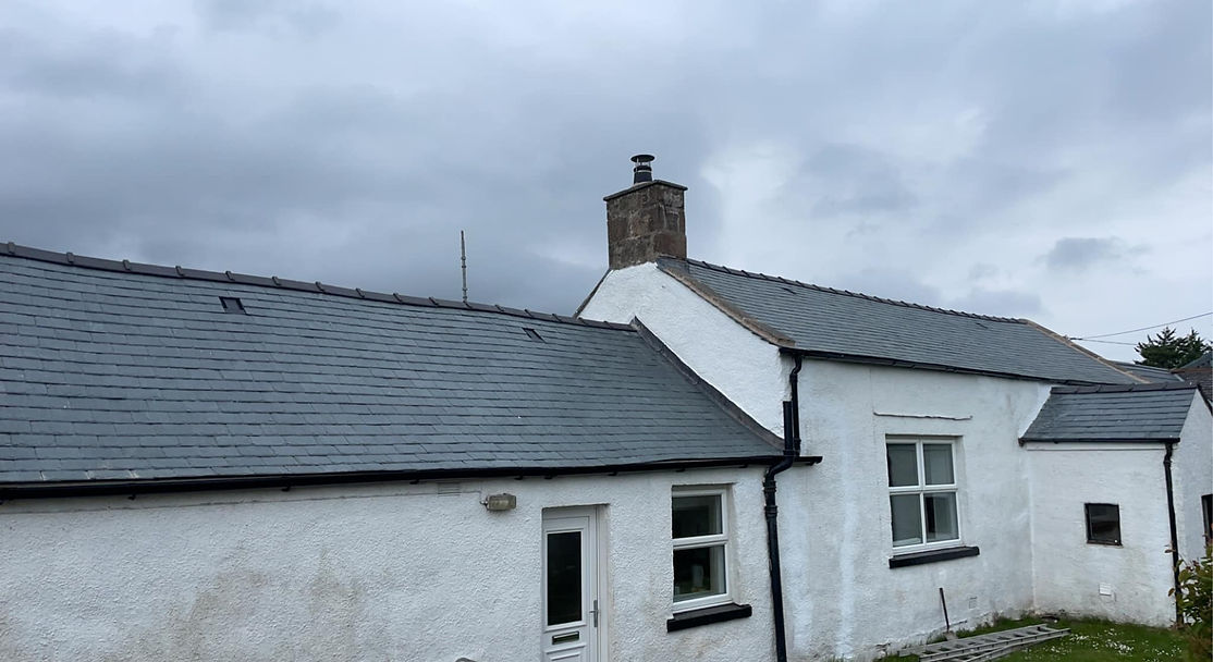 A white cottage with a slate roof sits under a cloudy sky