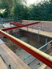 Red steel RSJ beams installed on top of a brick house extension with internal scaffolding in the UK