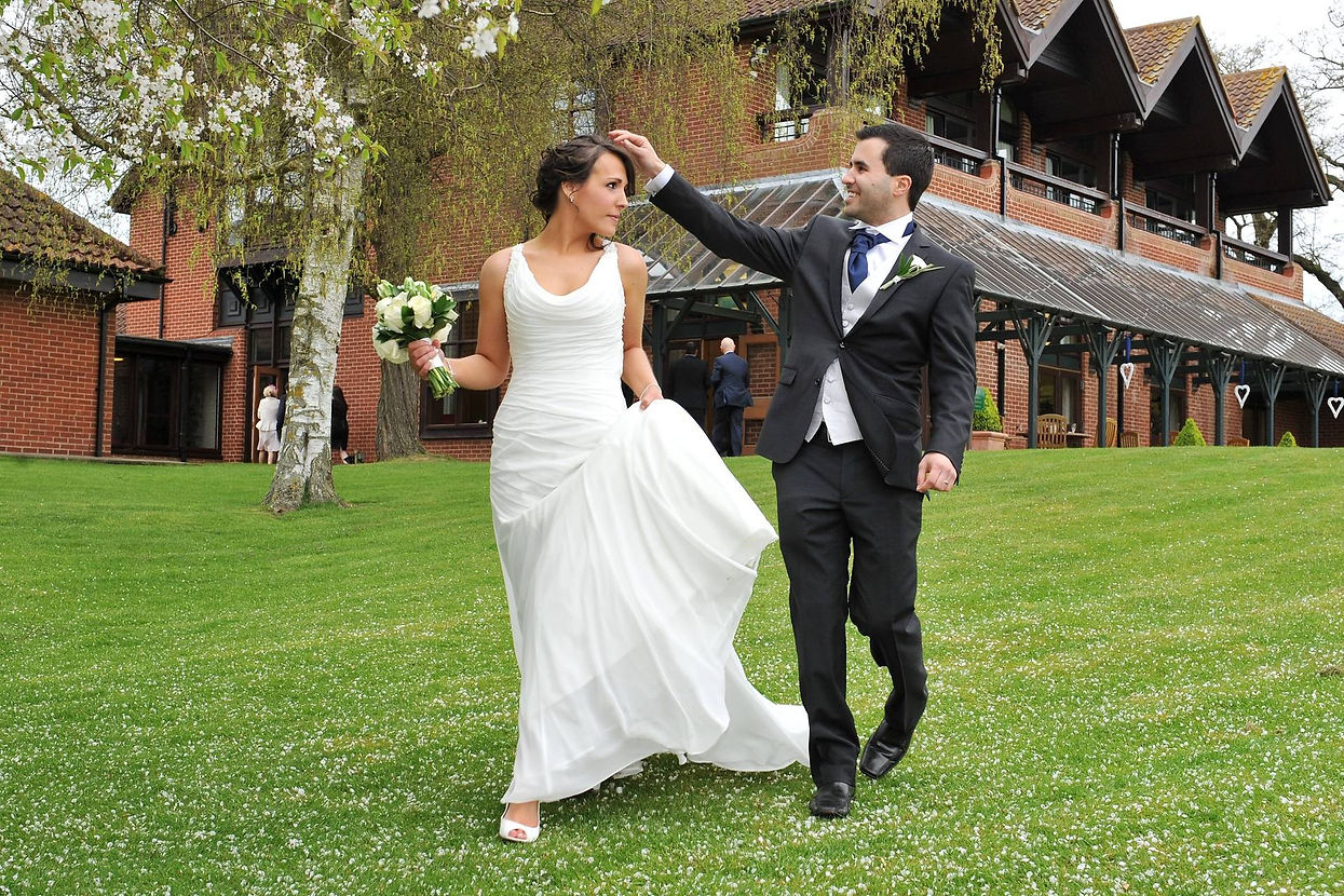 A bride and groom joyfully walk on a green lawn in front of a brick building