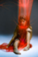Woman sitting on the floor behind a red sheer fabric, creative portrait on film and dance photography with tulle fabric