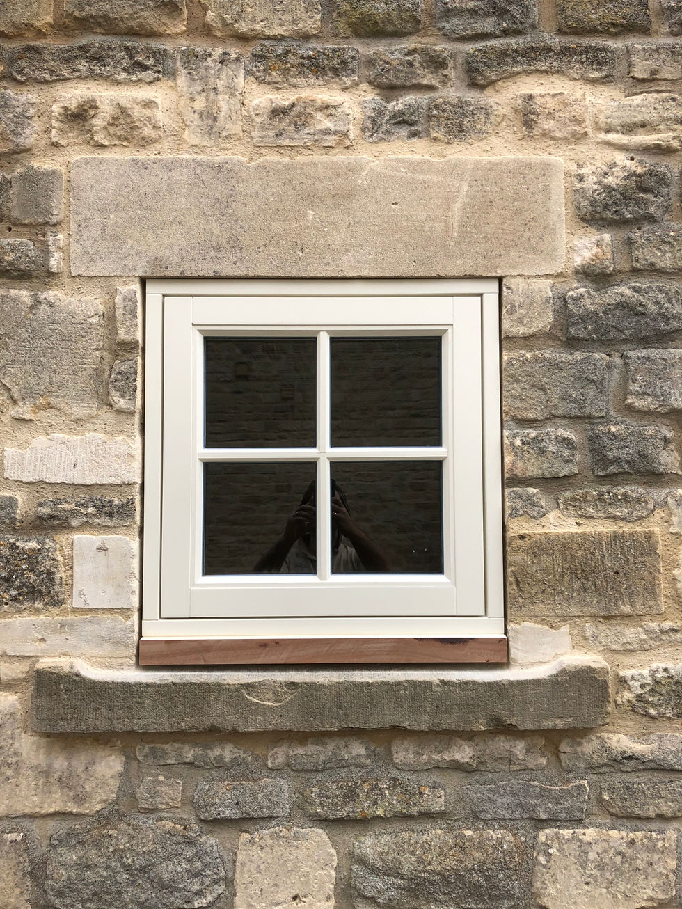 Newly installed hardwood sash window with wrought ironwork furniture in a Cotswold cottage.