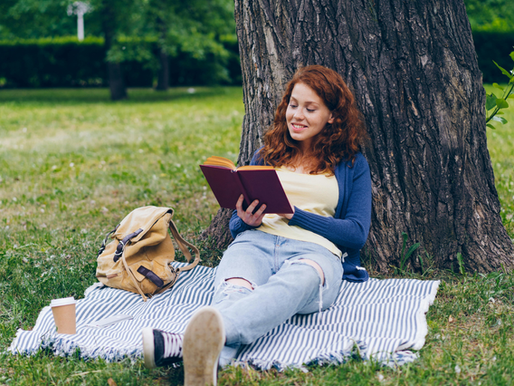 Pessoa sentada sob uma árvore lendo um livro em um ambiente tranquilo e cercado pela natureza.