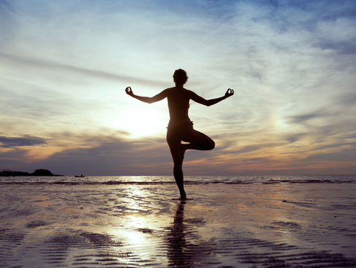 Mulher em pose de yoga de equilíbrio em frente a uma praia com um lindo pôr do sol.
