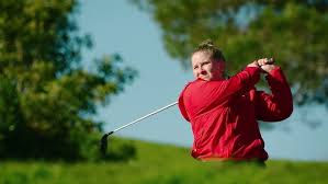 A white woman swinging a golf club wearing a red jacket.