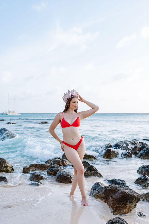 Miss Aruba Teen posing in a red bikini with a crown on the shoreline at Arashi Beach Aruba during a solo photoshoot captured by Edrxck