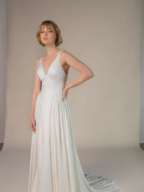 Simple silk A-line wedding dress with deep V-neckline and shoulder straps, featuring a dropped waist, flowing silk skirt, and sweeping train, styled as a vintage-inspired minimalist wedding gown.