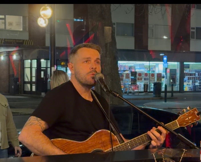 Man playing guitar and singing live in a cozy evening street-side setting