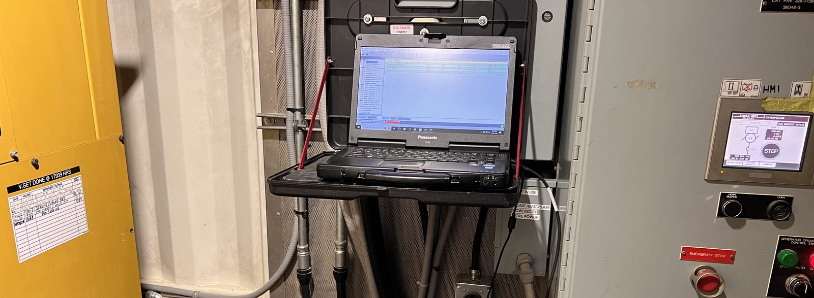 Laptop on a stand connected beside a generator control panel