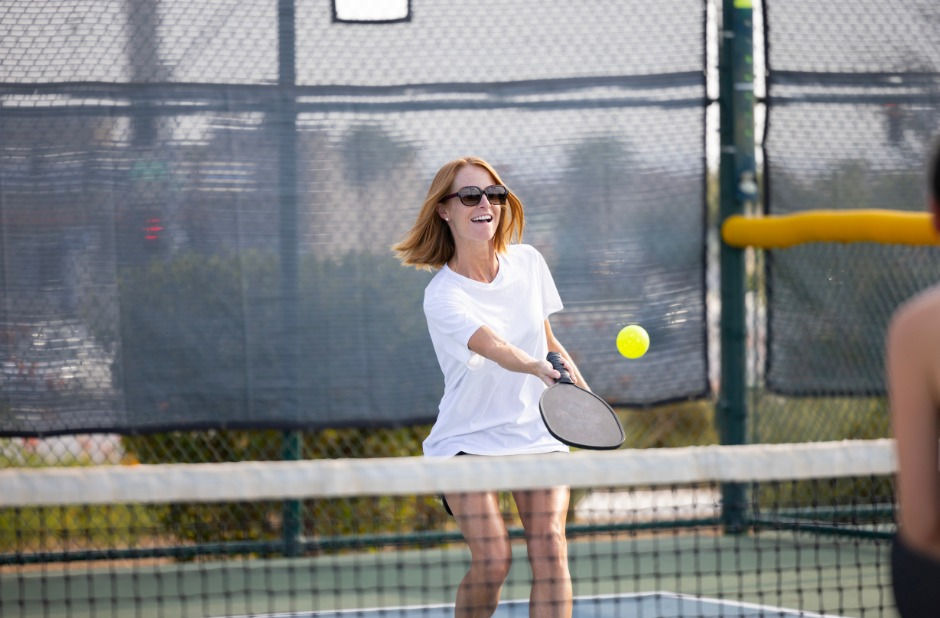 A woman smiling and playing pickleball.