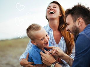 Family of three laughing outdoors, parents tickling a young boy. Blue sky, grassy field background. Drawn white hearts suggest happiness.