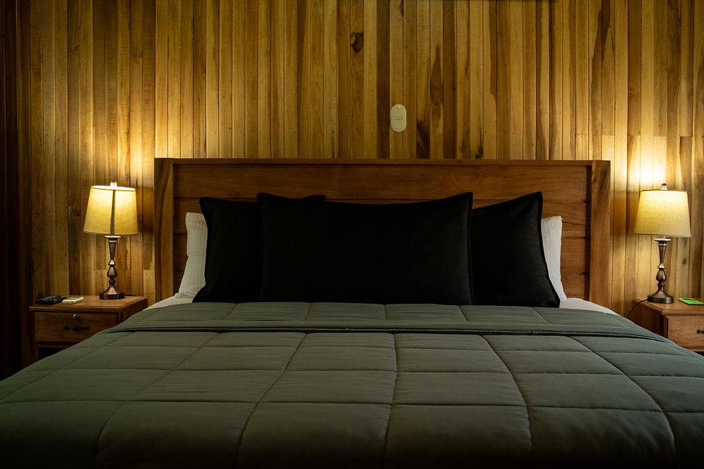 Dormitorio con cabecero de madera, cama y lámparas encendidas.