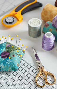 Scissors, thread, pin cushion,and other sewing notions on a sewing table.