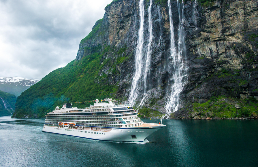 Viking ocean ship sailing past tall waterfalls cascading down a cliff in a Norwegian fjord