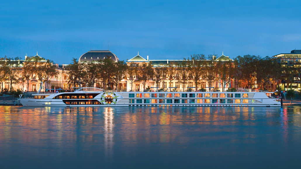 Tauck ms Emerald docked at twilight, its lights reflecting on the water in front of a grand illuminated building
