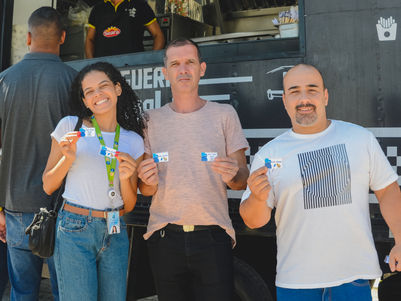 Three people smiling and holding tickets near a food truck, outdoors.