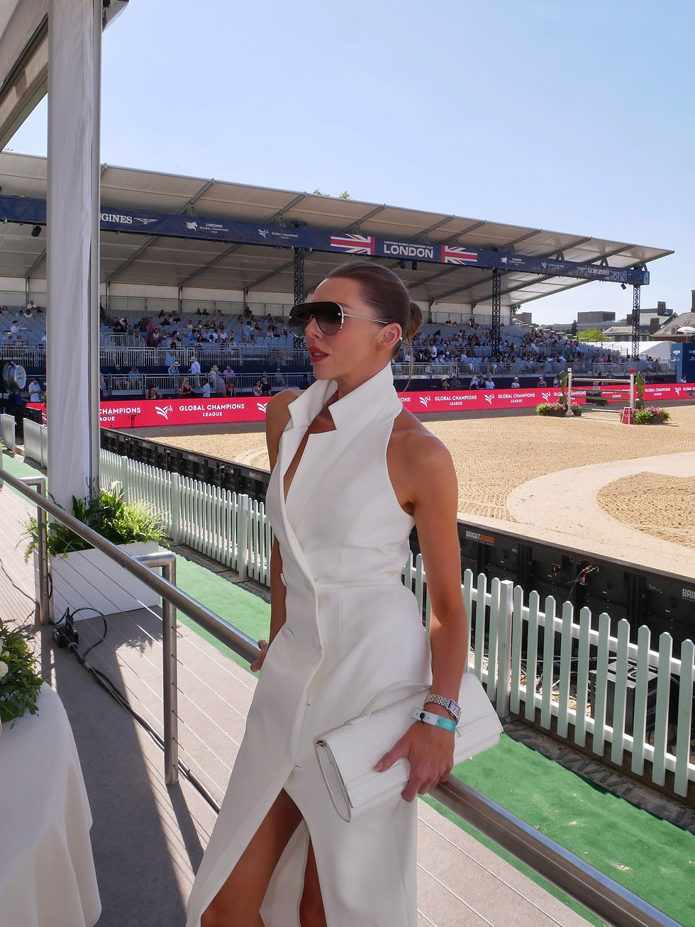 Laura Blair attending the Longines Global Champions Tour in Chelsea as a guest of Longines, wearing a white waistcoat style backless summer dress and the Longines Mini DolceVita Quartz watch in stainless steel with an 18 karat yellow gold crown, alongside images of the show jumping, elegant outdoor dining, food, drinks and quintessential British summer atmosphere.