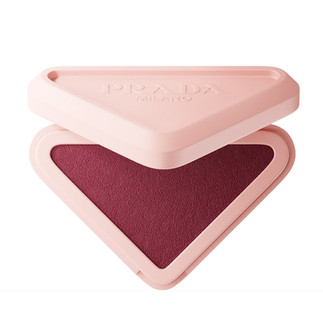 Soft mauve-berry Prada blush in a sleek triangular compact with pale pink packaging and embossed Prada Milano logo, shown with velvety powder texture and rosy plum pigment in a luxury editorial beauty style.