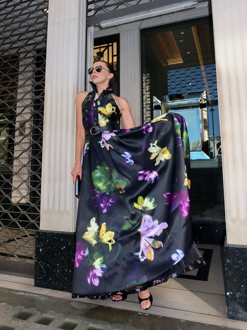 Laura Blair wearing a Karen Millen black floral woven twill collared maxi dress with a halterneck, defined waist and full flowing skirt, styled with a black underskirt and black heeled sandals outside in London.