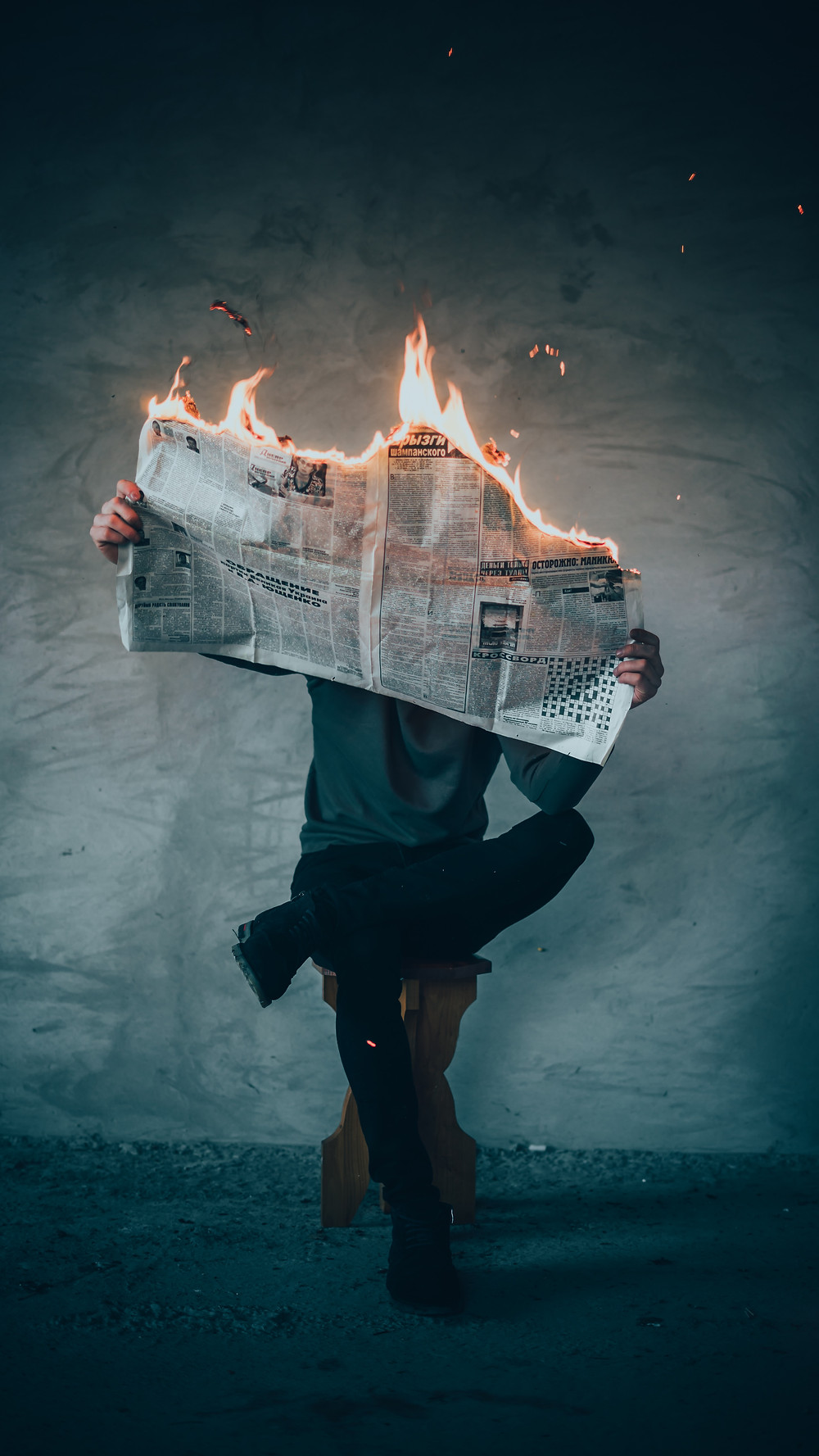seated person holding a burning newspaper that hides the face