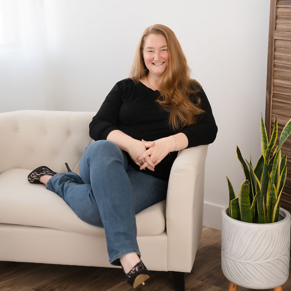 Meghan casually sitting on a white couch, wearing a black shirt, blue jeans and black heels