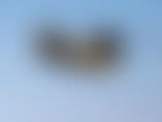 Askerde, yeşil-kahverengi kamuflajlı bir helikopter uçuyor. Gökyüzü açık mavi, helikopter havada asılı.
