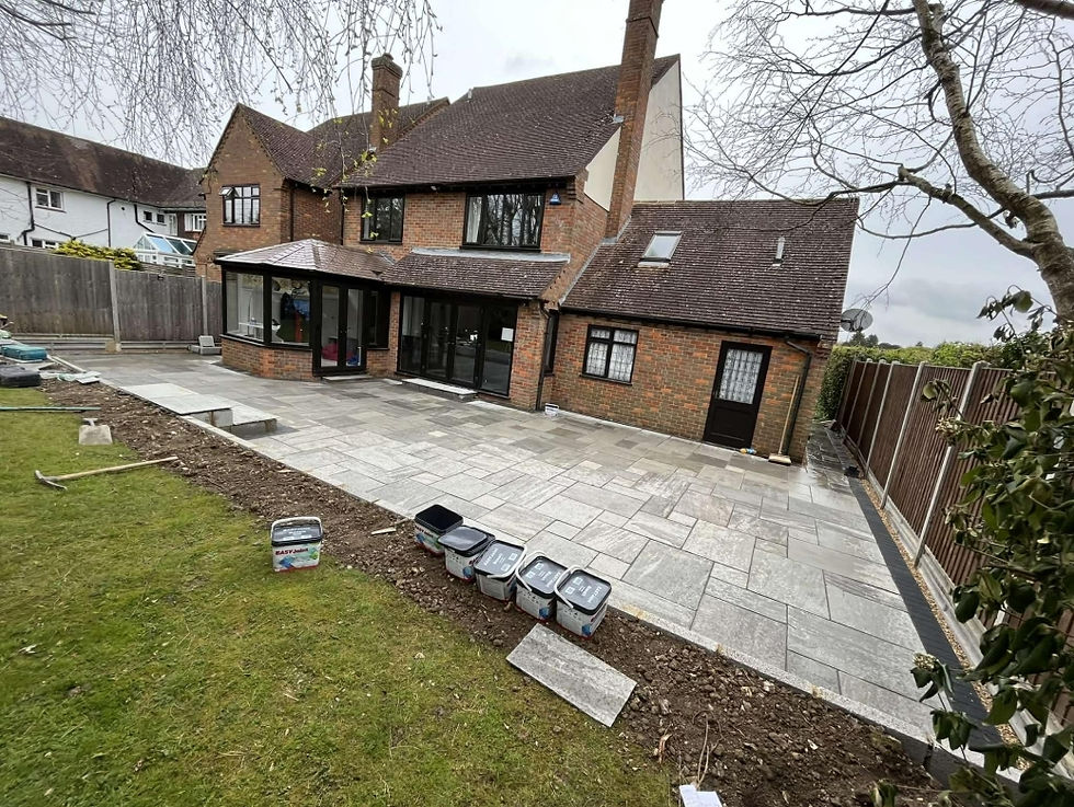 Large new grey patio behind a brick house with a green lawn.