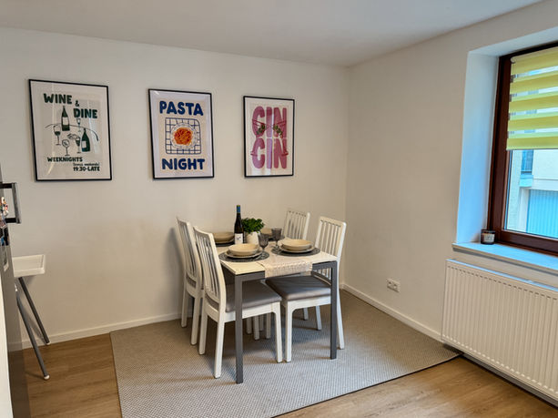 Essbereich mit rundem Tisch, weißen Stühlen, Blumen und Wandpostern wie 'Wine & Dine', 'Pasta Night' und 'Gin'