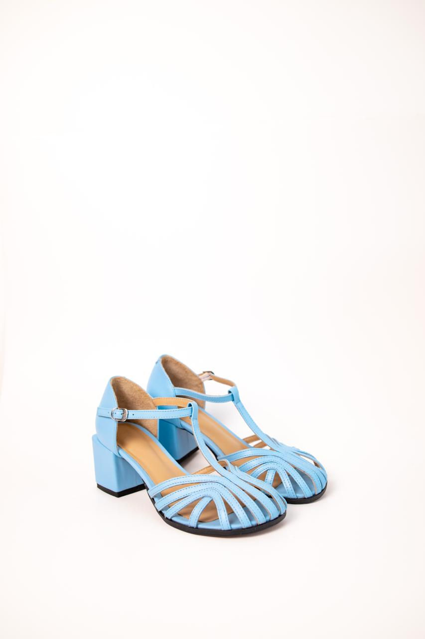 Miniatura: Błękitne sandały damskie o fasonie pajęczyny trzymane w dłoniach na tle czerwonej sukienki