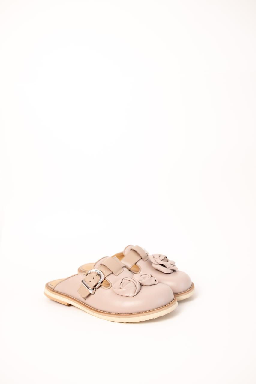 Miniatura: Beżowe chodaki skórzane z dużymi różami 3D i metalową klamrą, trzymane w dłoni na tle czerwonej sukienki.