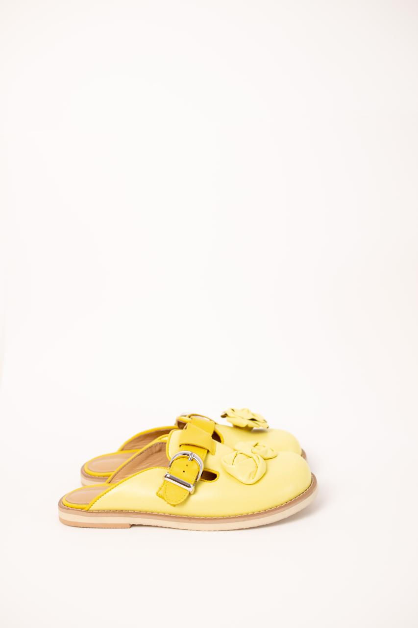 Thumbnail: Kobieta prezentuje skórzane chodaki z trójwymiarową różą na kamiennej ścieżce, widok na artystyczny detal.