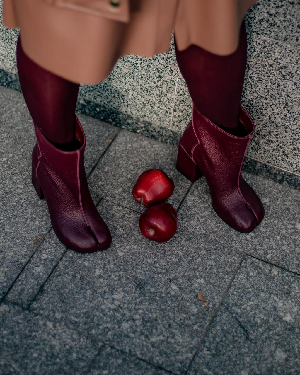 Бордові шкіряні ботильйони табі на високих підборах на фоні гранітної плитки з червоними яблуками.