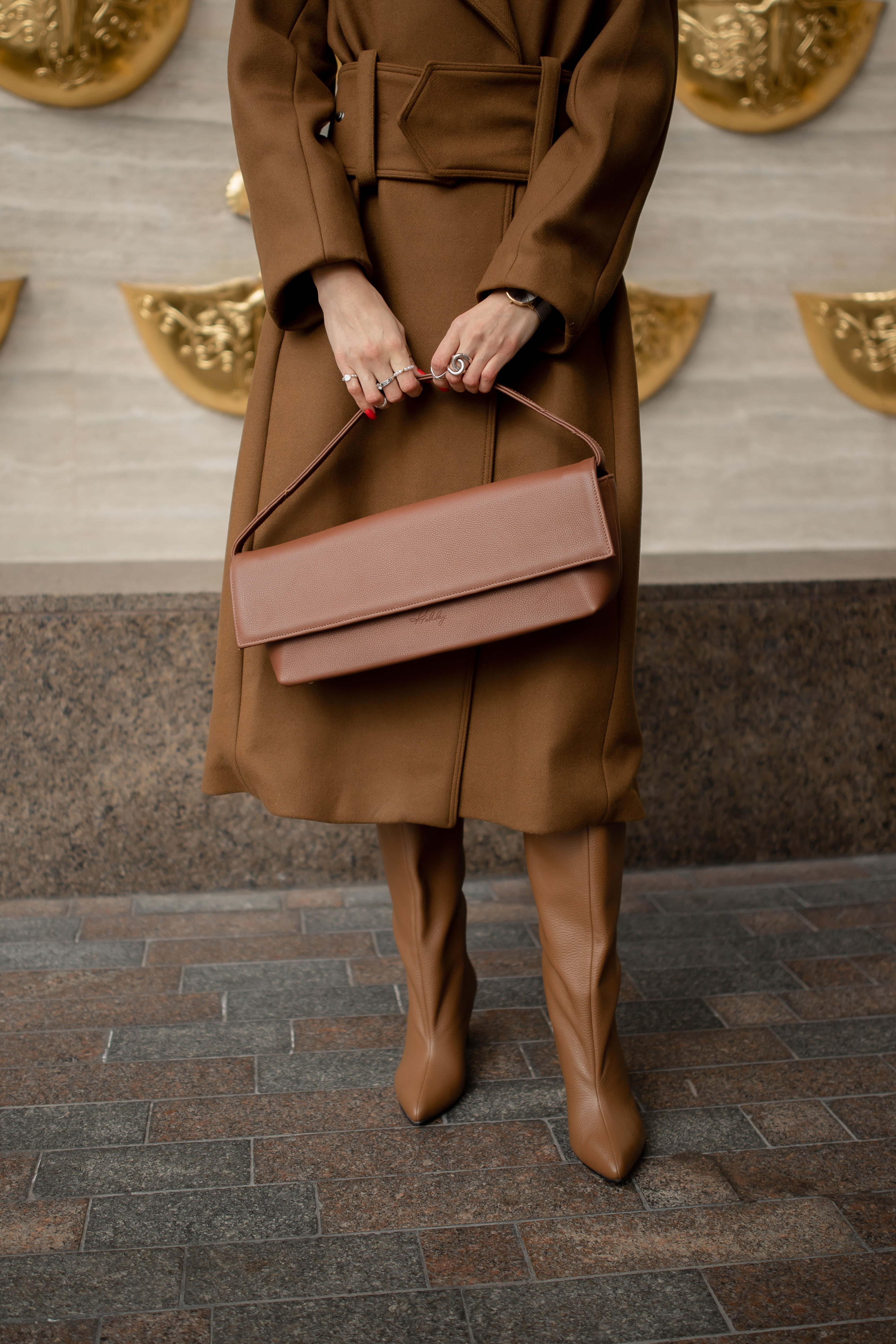 Жіноча коричнева шкіряна сумка у формі клатча в руках жінки в кашеміровому пальто.