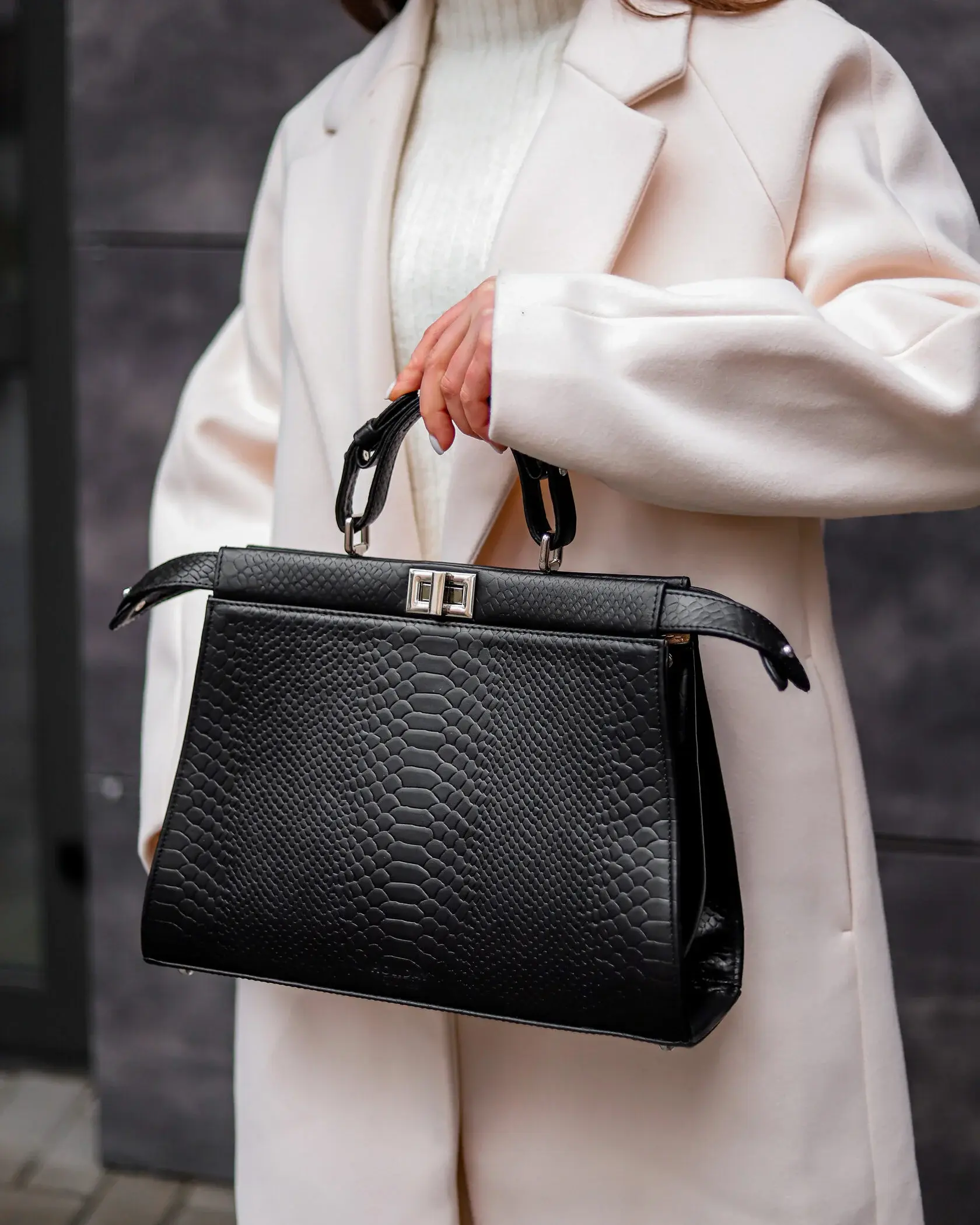 Чорна дизайнерська сумка з текстурою пітона на темному фоні.