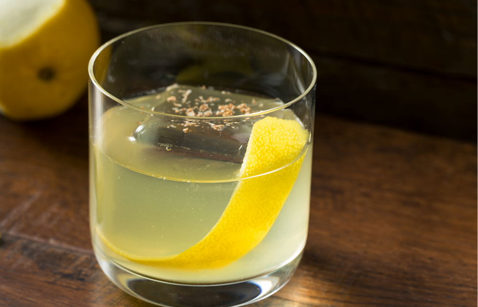 A class showing a clarified milk punch served with lemon peel and nutmeg