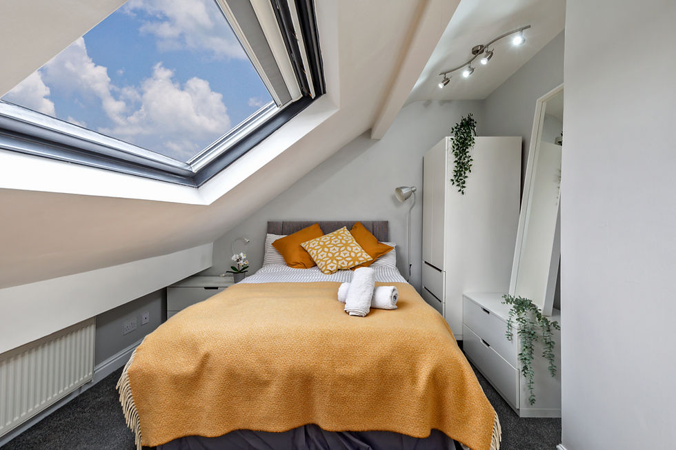 Cozy attic bedroom with skylight, bed with orange pillows and blanket, white cabinets, and potted plants, creating a warm, inviting space.