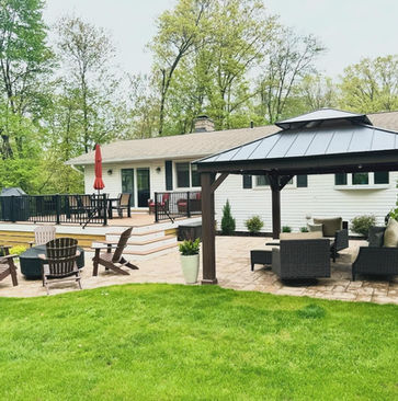 Custom backyard outdoor living space with elevated deck, black railings, fire pit patio, gazebo lounge area, and landscaped yard in Rockland County NY by Peluso Construction.