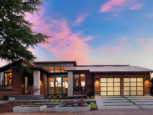 Modern house with large windows and garage at sunset. Clouds and a blue sky in the background create a serene atmosphere.