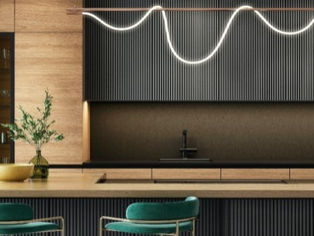 Modern kitchen with sleek wood cabinets, wavy pendant light. Two teal barstools and a bowl on the island.