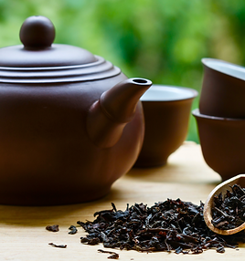 紫砂茶壺與茶杯擺放在木質桌面上,旁邊散落著烏龍茶葉,呈現傳統台灣茶文化的品茗情境。A Yixing clay teapot and teacups placed on a wooden table with loose oolong tea leaves, showcasing the essence of traditional Taiwanese tea culture.