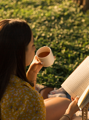 A woman enjoying tea while reading outdoors, symbolizing the nutrition and wellness benefits of NAK’s Taiwan tea, naturally rich in polyphenols, amino acids, and antioxidants for global consumers.