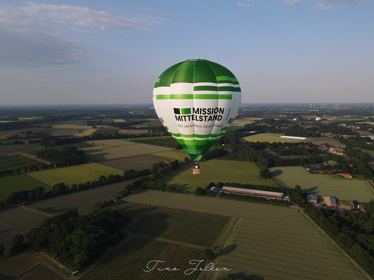 Der grüne Mission Mittelstand Ballon fliegt über Felder.