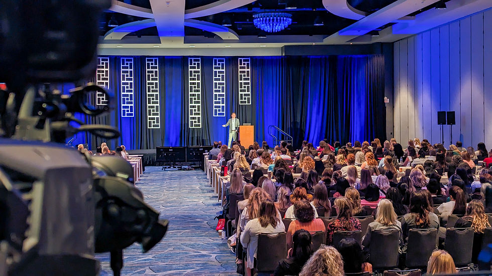 Video camera at back of room filming a general session presenter at a conference