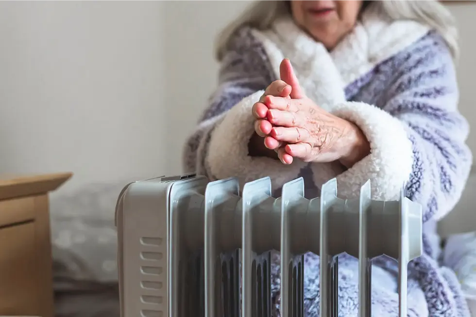 Personne âgée se réchauffant les mains près d’un radiateur à domicile en hiver, illustrant les risques liés au froid et au confort thermique des seniors