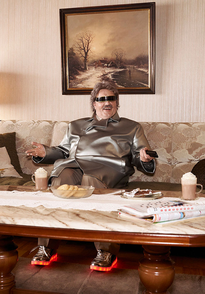 Man in silver tracksuit sitting on vintage living room sofa, retro styled cinematic scene.
