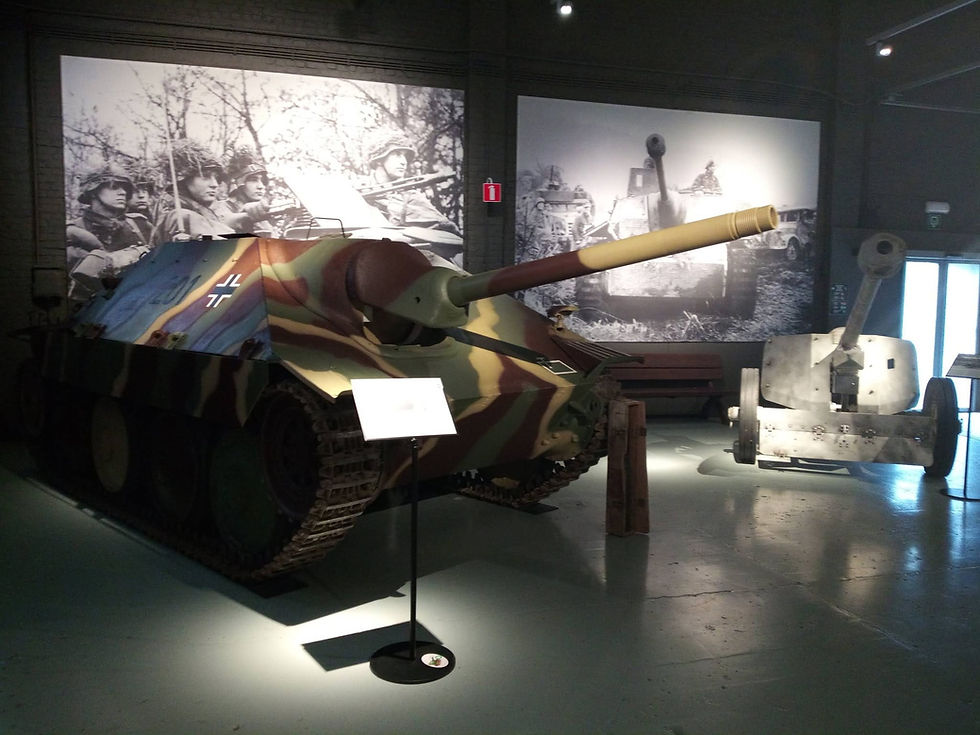 Panzer in Militärmuseum: getarnter Kampfpanzer mit langem Rohr vor Schwarzweiß-Fotos, daneben ein Geschütz.