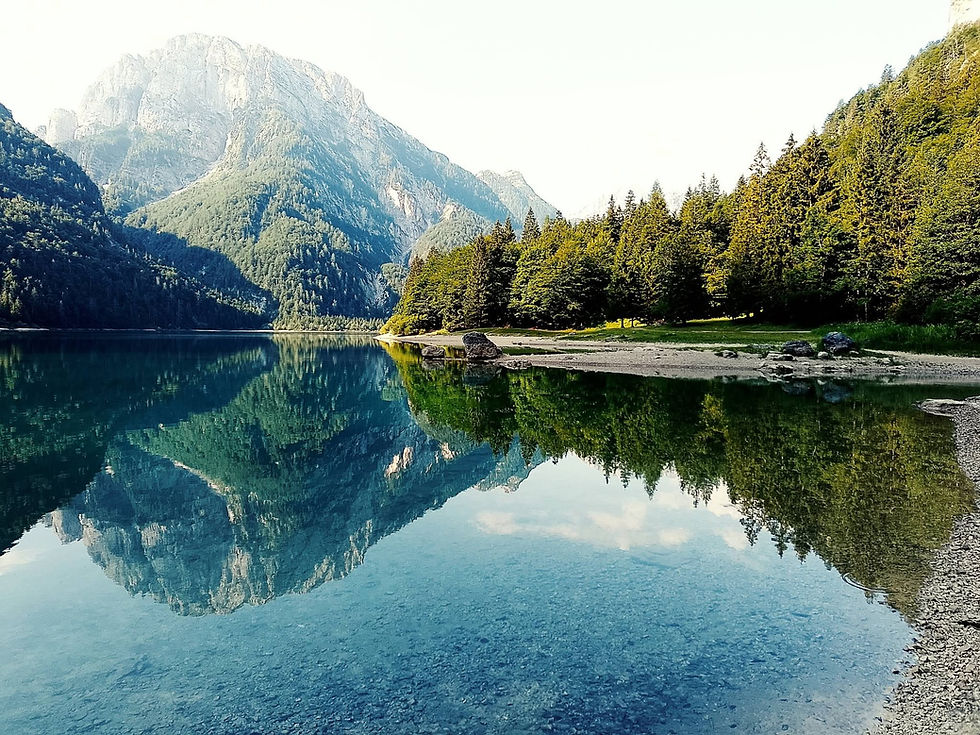 Bergsee Lago del Predil mit spiegelglatter Oberfläche, Tannenwald und steilen Felsen; klares Wasser reflektiert die Berge.