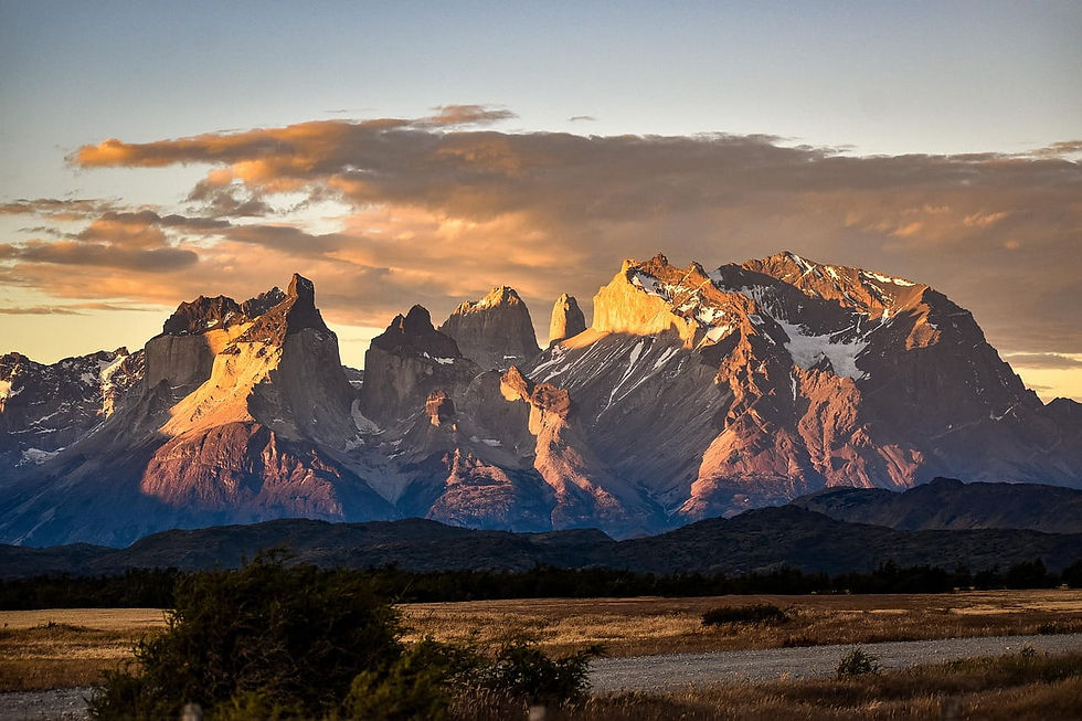Gebirgskette bei Sonnenuntergang mit schneebedeckten Gipfeln, goldene Wolken am Himmel, Grasland im Vordergrund. Ruhevolle Stimmung. Reiseziel Chile