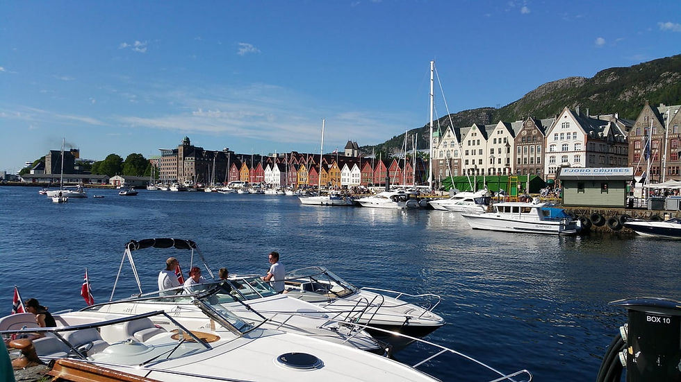 Hafen in Bergen mit Yachten, bunten Giebelhäusern und Bergen unter blauem Himmel; Schild Fjord Cruises am Kai.