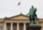 Reiterstatue vor klassischem Gebäude mit weißem Säulengiebel; oben weht die norwegische Flagge.