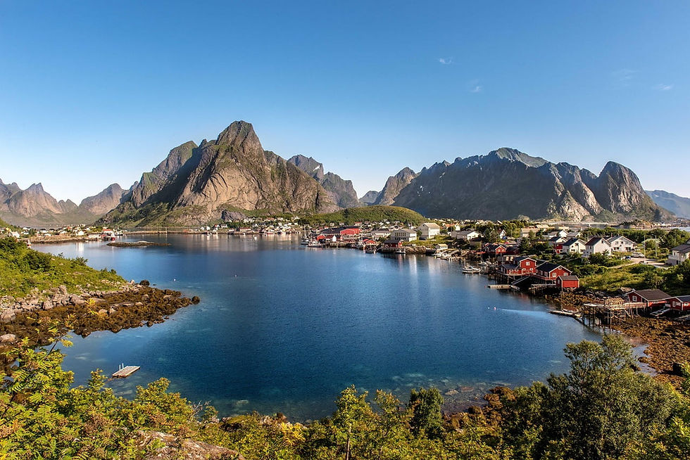 Fjord mit roten und weißen Häusern auf den Lofoten, ruhiger blauer Bucht und schroffen Bergen unter klarem Himmel.